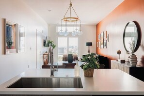 A modern kitchen with a large island, a hanging light fixture, and a view of the city. - Gallery Retreat | Skyline Views | Zuni Lofts (Denver)