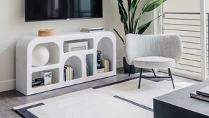 Una sala moderna con una televisión de pantalla plana montada en una consola blanca, un sillón gris y una planta grande en maceta.