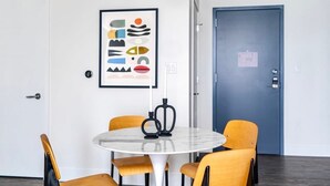 Una habitación moderna con una mesa redonda, cuatro sillas, una obra de arte abstracta enmarcada y una puerta azul.