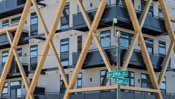 Un bâtiment moderne doté d’une structure triangulaire en bois originale, de nombreux balcons et d’un panneau de signalisation indiquant « 29th Ave » et « Zuni St ».