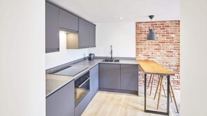A modern kitchen with grey cabinets, a wooden table, and a brick accent wall. - Host & Stay | Modern Industrial (Whitby)