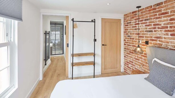 A bedroom with a bed, a wooden door, a brick wall, and a window. - Host & Stay | Modern Industrial (Whitby)