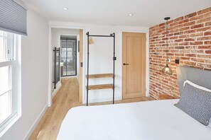 Quarto com cama, porta de madeira, parede de tijolos e janela.
