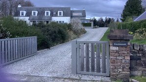 En grusuppfart leder fram till en grindad entré med en mur av sten och en skylt med texten ”Knockinreoch”.