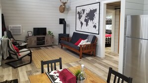 Ein gemütliches Wohnzimmer mit einer Couch, einem Esstisch und einem Fernseher. An der Wand hängt eine Weltkarte und es gibt einen Deckenventilator.