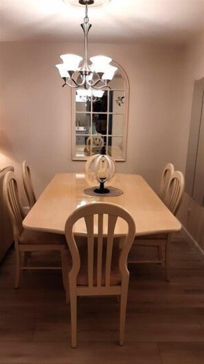 A dining area with a table, chairs, a chandelier, and a mirror on the wall. - Sand Pebbles #1401 Chateau La Mer II 2Bd-2Bath Walk-In Shower Ground Floor (Destin)