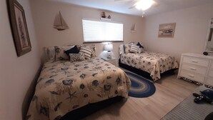 Un dormitorio con dos camas, un aparador, un ventilador de techo y una ventana con persianas.