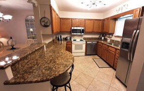 A kitchen with granite countertops, wooden cabinets, stainless steel appliances, and a dining area with a table and chairs.