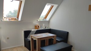 Ein kleiner, moderner Raum mit schrägem Dach, einem Holztisch mit Papieren, einer schwarzen Couch und einer Bank.