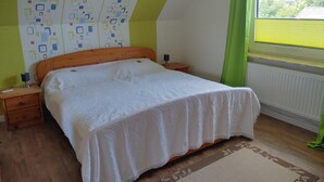 Ein Schlafzimmer mit einem hölzernen Bett, einem Nachttisch mit Lampe, einer Wand mit Muster und einem Fenster mit Jalousien.