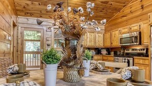 A rustic wooden cabin interior with a dining area, a kitchen with modern appliances, and a decorative centerpiece. - Relaxing Cabin Getaway! HOT TUB! Large Yard! Wifi (Sevierville)