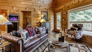 A cozy cabin interior with a leather sofa, a round coffee table, and a TV displaying 'Ultracade'. - Relaxing Cabin Getaway! HOT TUB! Large Yard! Wifi (Sevierville)