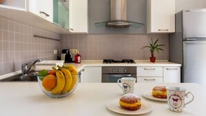 Eine moderne Küche mit weißen Schränken, einem Gasherd und einer Edelstahl-Dunstabzugshaube. Auf der Arbeitsplatte befinden sich eine Fruchtbowl und zwei Gebäckstücke.