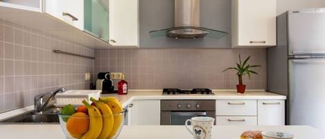 A modern kitchen with white cabinets, a gas stove, and a stainless steel range hood. There is a bowl of fruit and two pastries on the counter.