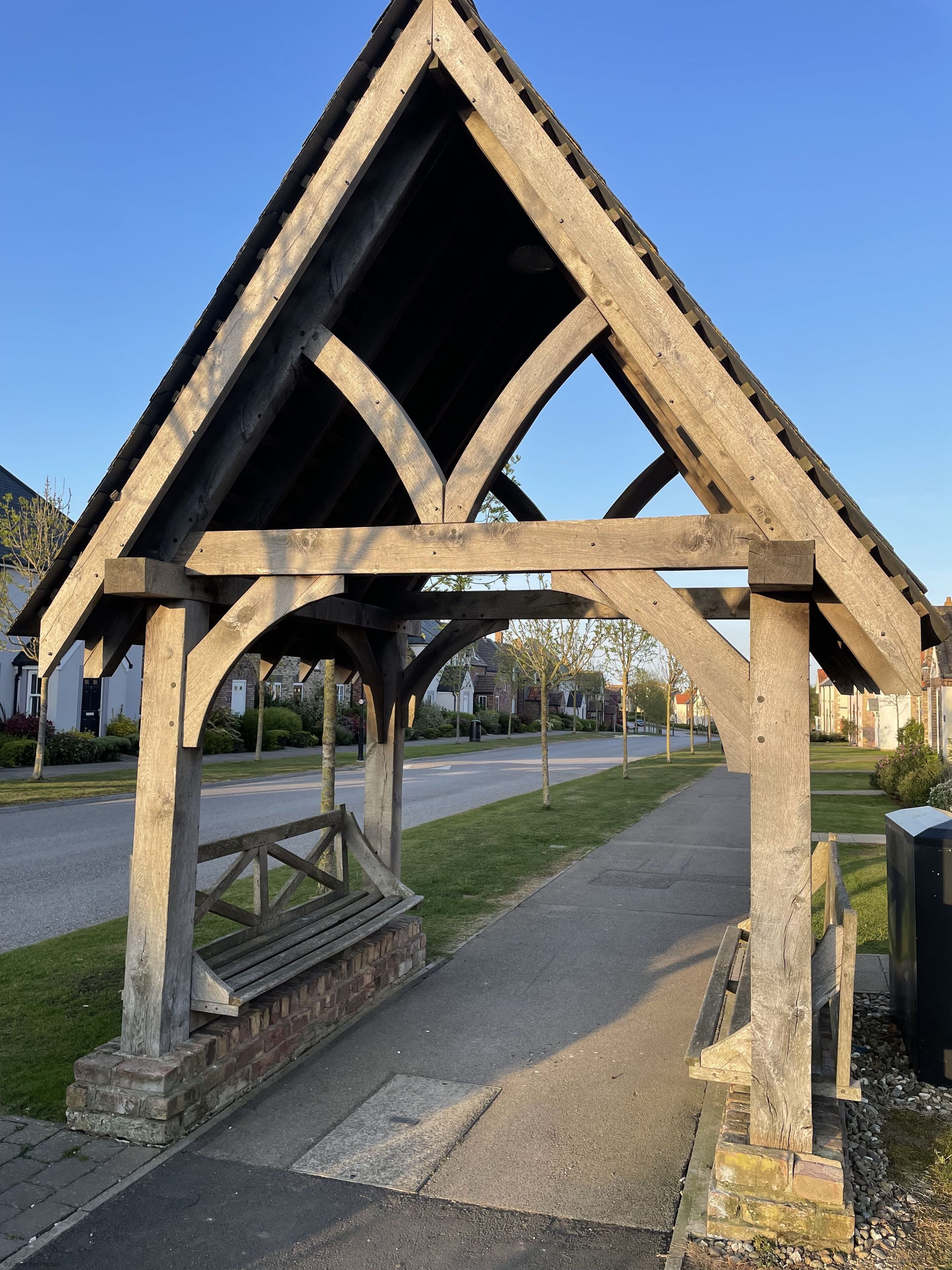 A wooden gazebo with a sloped roof and a bench underneath.