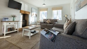 Ein gemütliches Wohnzimmer mit Kamin, einer Couch, einem Couchtisch und einem flachbildfernseher an der Wand.