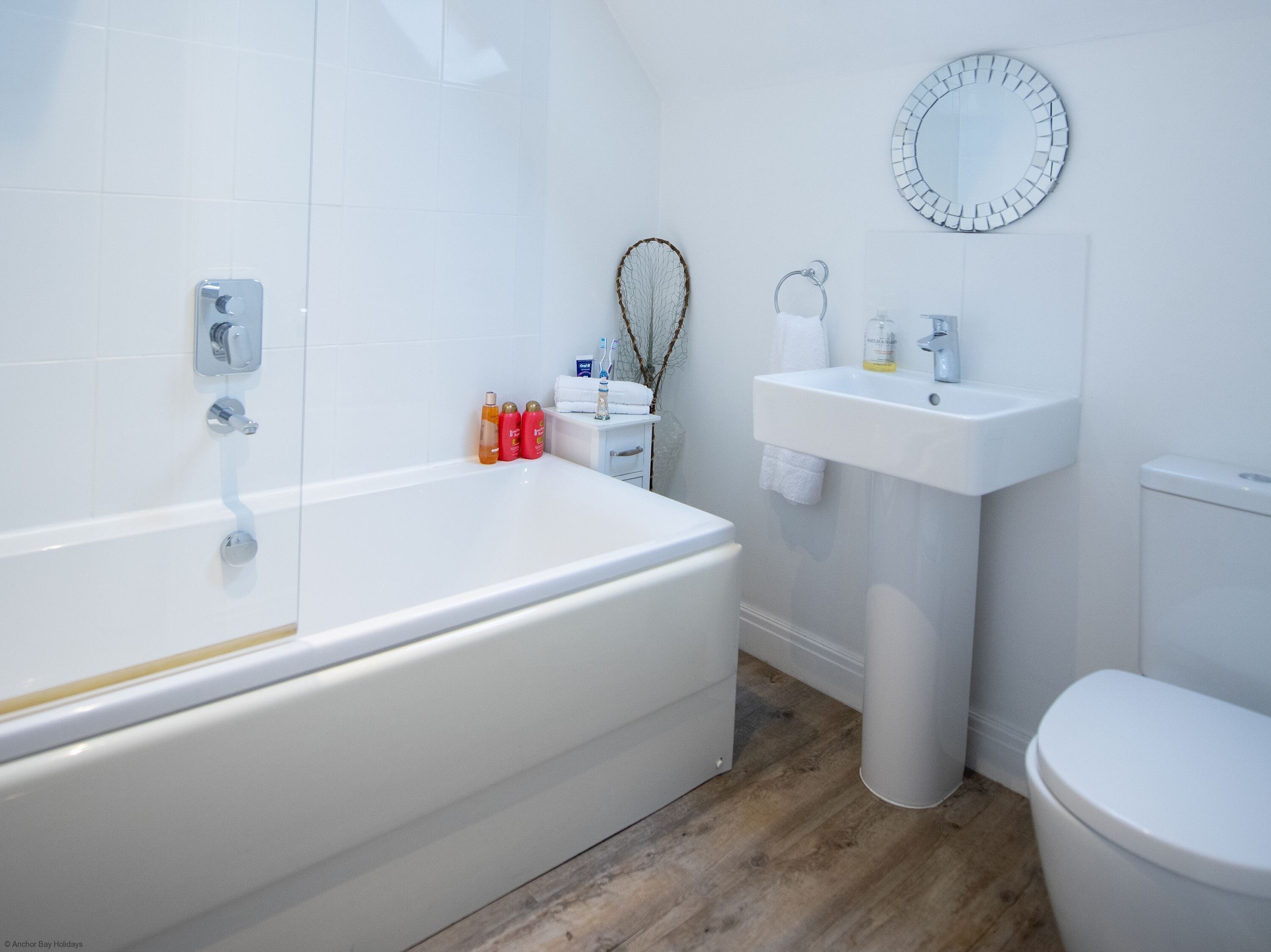 Une salle de bain moderne avec une baignoire blanche, un lavabo et des toilettes. On trouve des articles de toilette sur le bord de la baignoire.