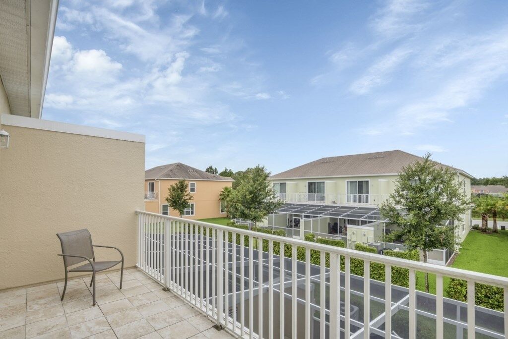 A balcony with a chair, a white railing, and a view of neighboring houses.