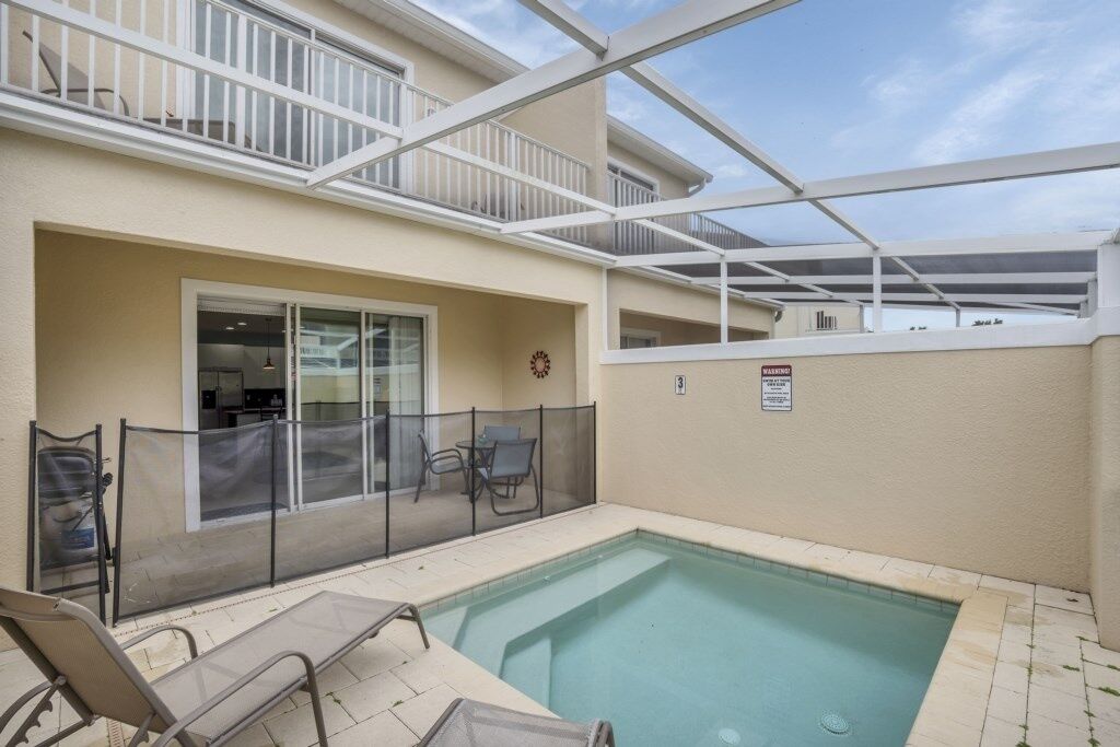 A pool area with a covered patio, a fenced enclosure, and a door leading to a building.