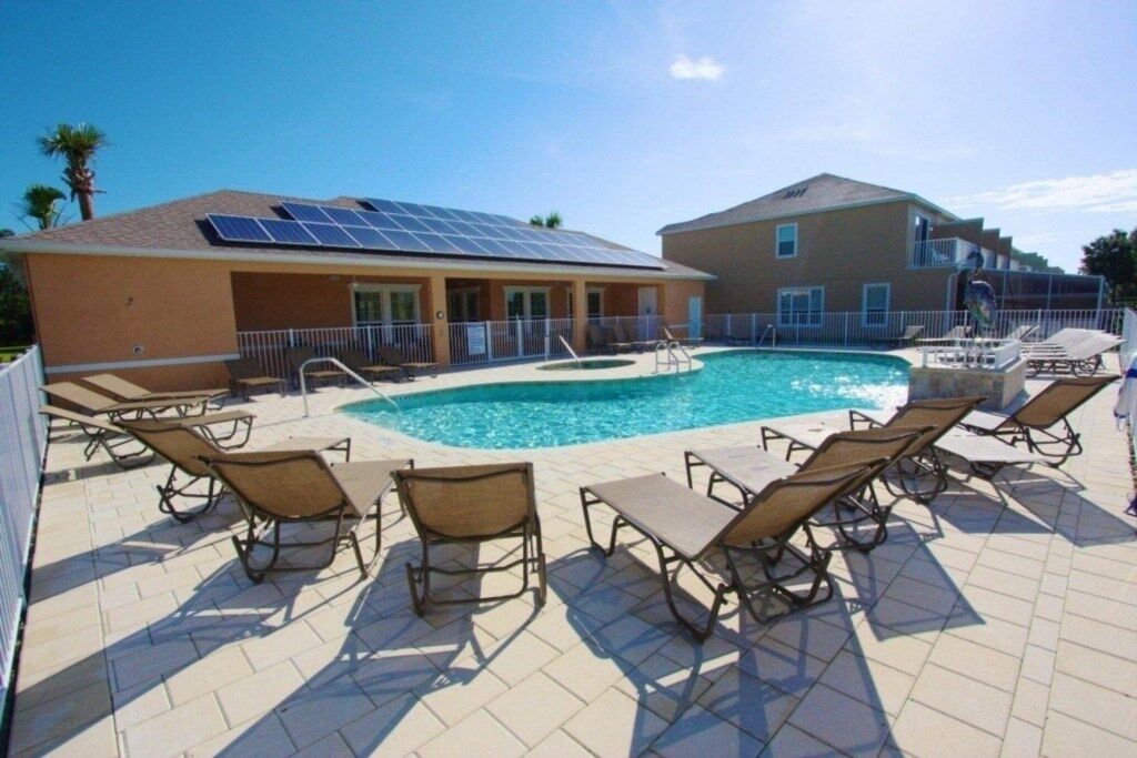 A swimming pool area with lounge chairs and a building with solar panels.