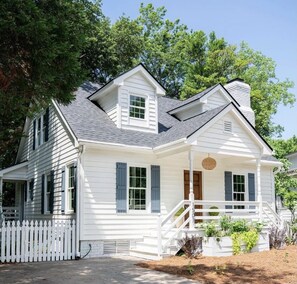A white two-story house with a porch, a chimney, and a picket fence.