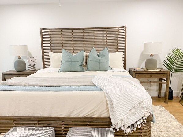 A neatly made bed with a wooden headboard, two bedside tables with lamps, a small plant, and a white throw blanket.