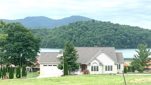 Une maison de plain-pied avec un garage, entourée d’une pelouse bien entretenue et d’arbres, avec un lac et des montagnes en arrière-plan.
