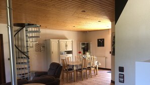 Un comedor con suelo de baldosas hexagonales, una mesa redonda y sillas de madera. Una escalera con barandillas de metal conduce a un nivel superior.