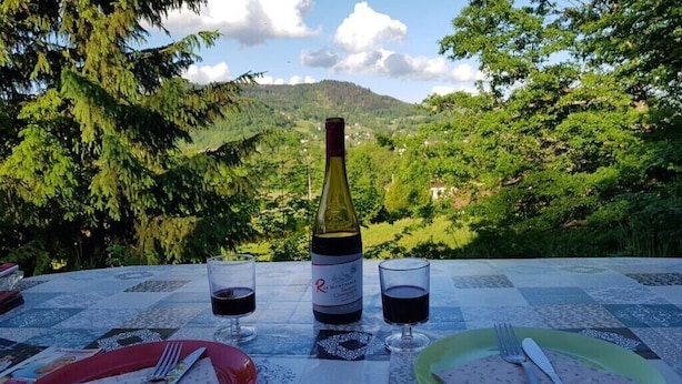 Mesa al aire libre con una botella de vino tinto, dos copas y platos con cubiertos.
