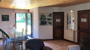 Una habitación con techo de madera, una zona de comedor con mesa y sillas, un sofá y una puerta que dice “CHAMBRE”.