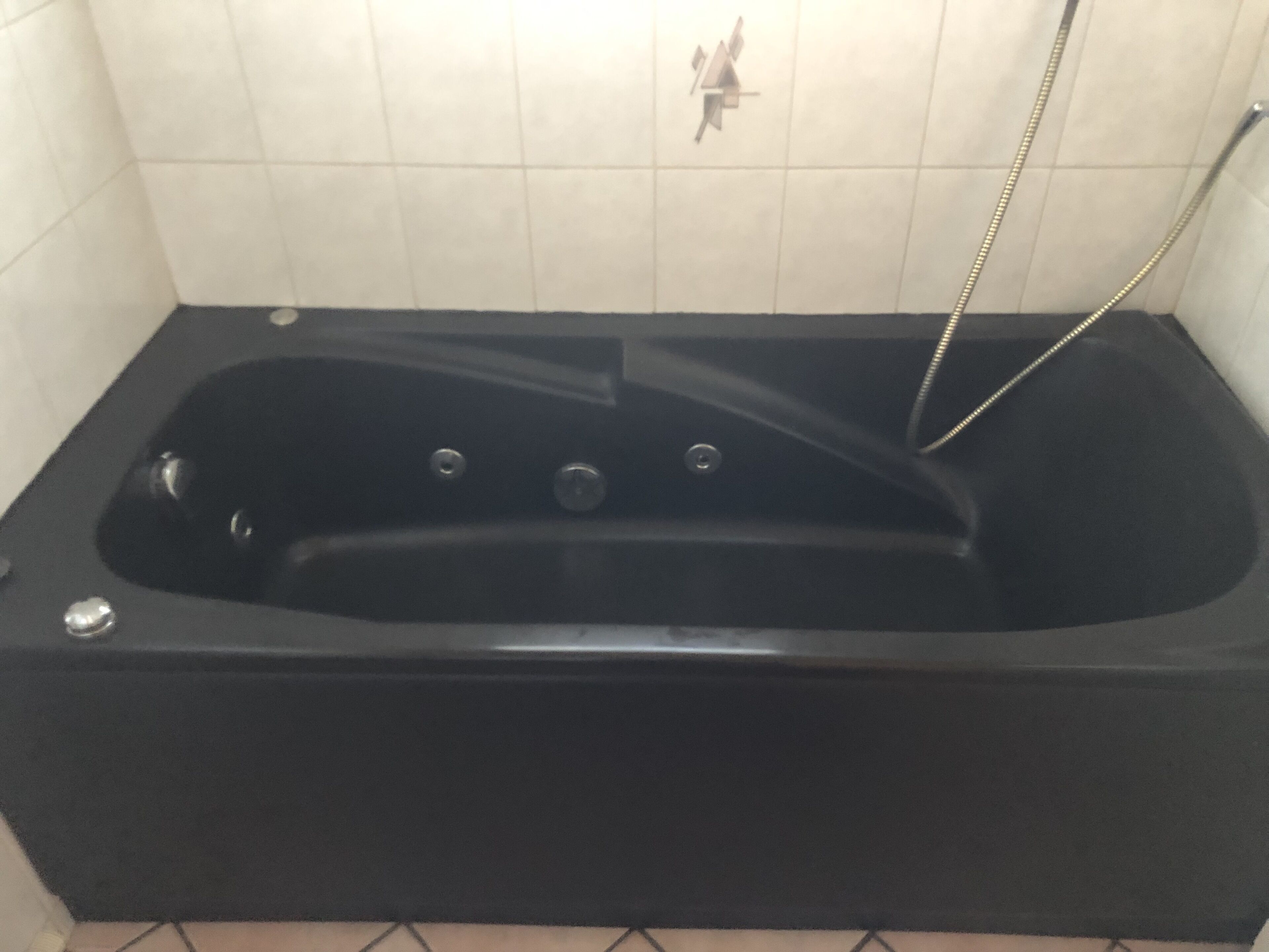 Une baignoire noire dotée d’un pommeau de douche à main, d’un robinet de commande et d’un drain.