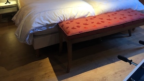 Un dormitorio con una cama grande, un banco, una mesita de noche y una puerta.