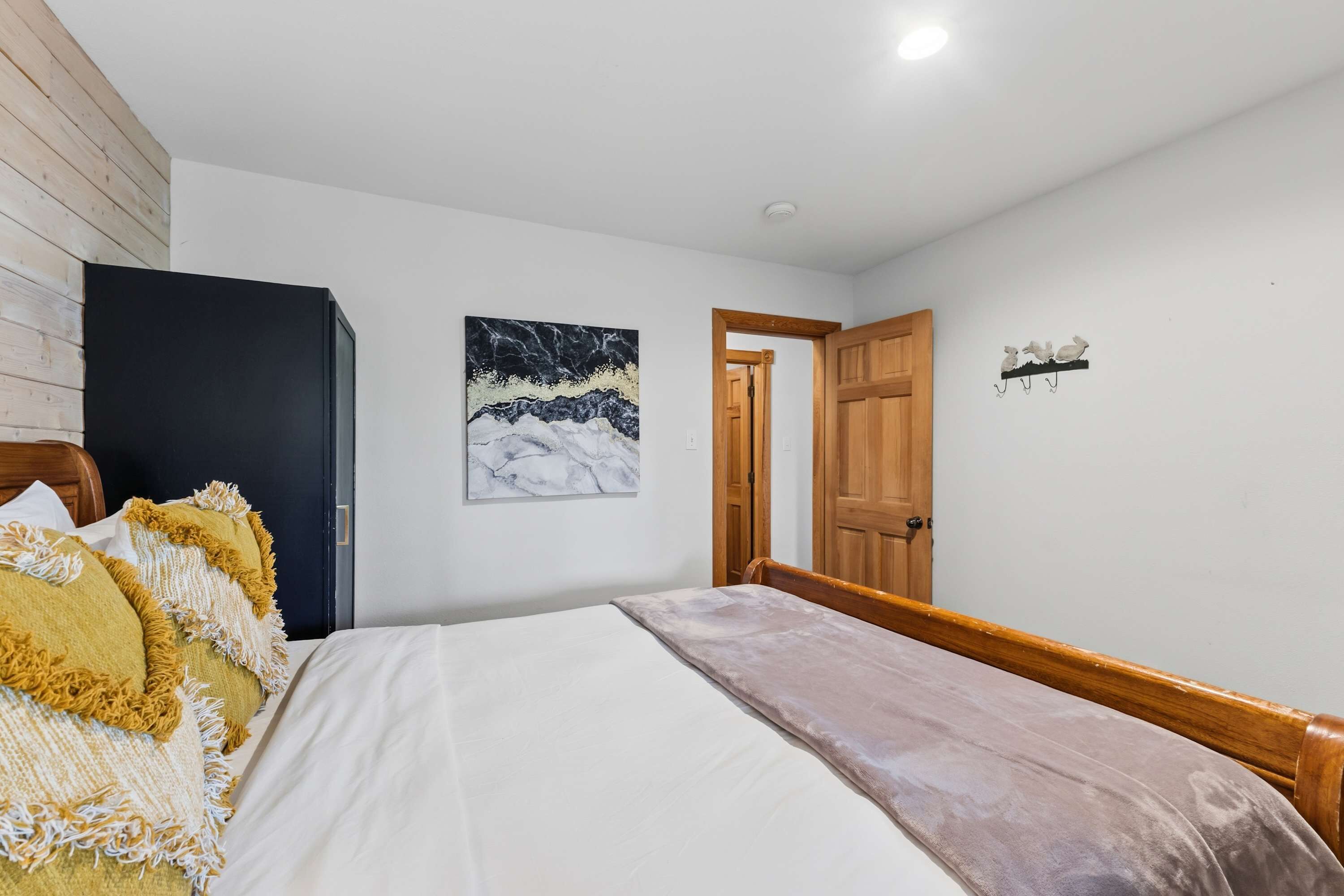 A bedroom with a bed, a wooden wardrobe, a door, and a wall-mounted artwork.