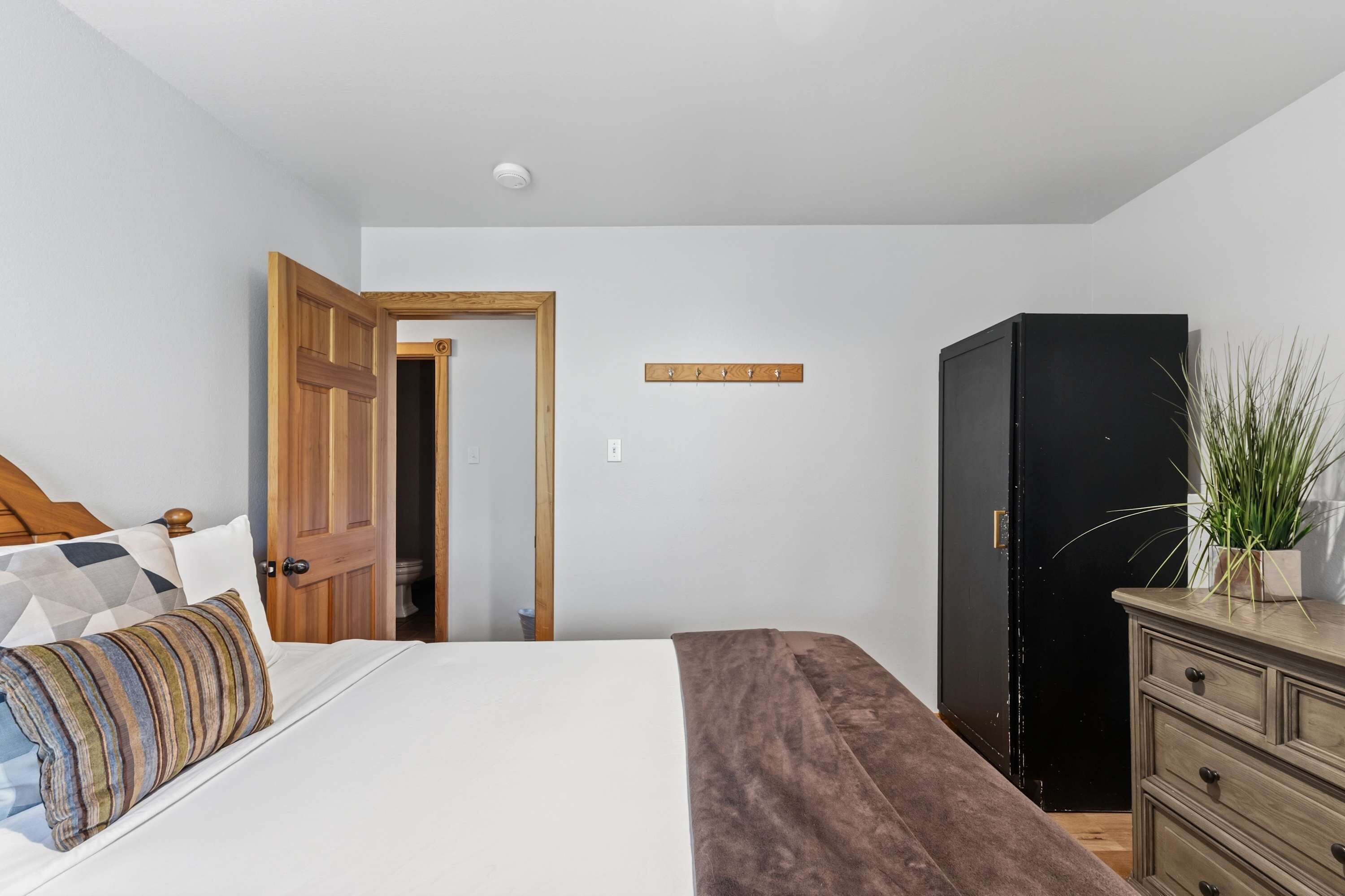 A bedroom with a bed, a wooden wardrobe, a dresser, and a door leading to another room.