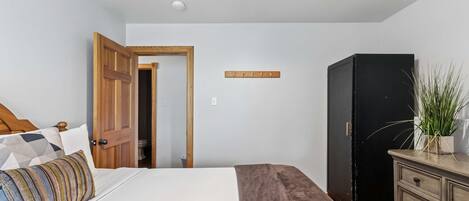 A bedroom with a bed, a wooden wardrobe, a dresser, and a door leading to another room.