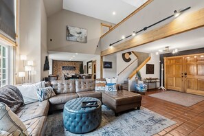 Un vaste espace de vie comprenant un grand canapé, un pouf et un escalier menant à un niveau supérieur.