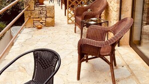 Een terras buiten met rieten meubilair, stenen muren en uitzicht op een berg.