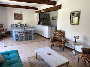 Een woonkamer met een blauwe bank, een houten salontafel, een fauteuil met bloemenprint en een eethoek met een blauwe tafel en stoelen.