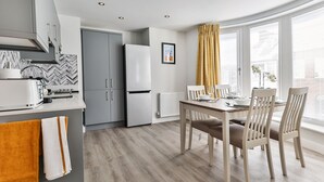 A modern kitchen with grey cabinets, a white refrigerator, and a dining area with a wooden table and chairs.