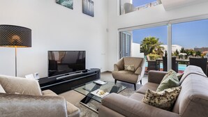 A modern living room with a flat-screen TV, comfortable seating, and a glass coffee table.