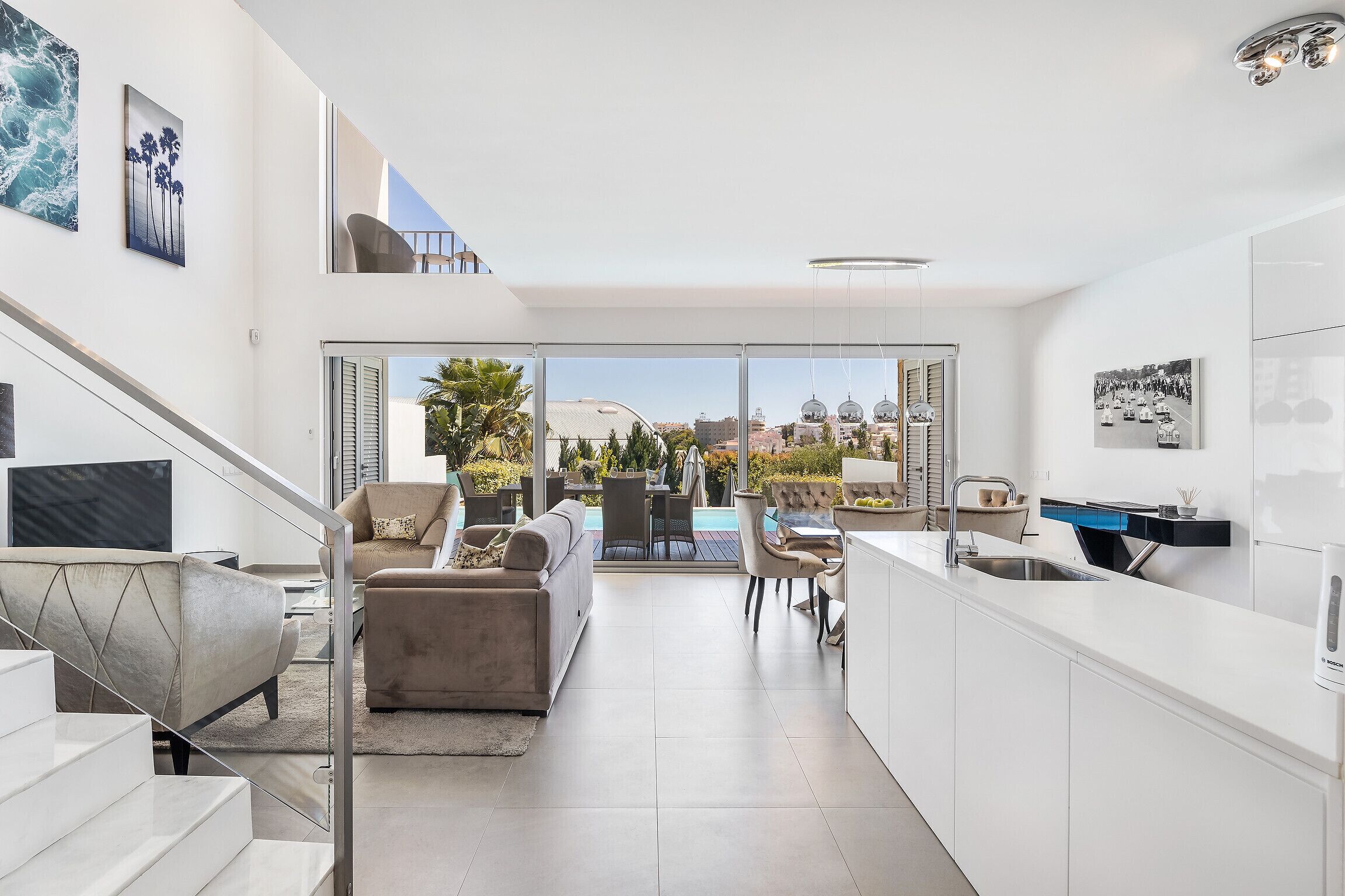 A modern kitchen with a large island, a dining area with outdoor seating, and a staircase leading to an upper level.