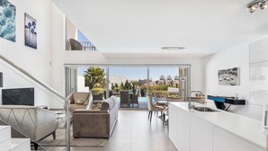 A modern kitchen with a large island, a dining area with outdoor seating, and a staircase leading to an upper level.