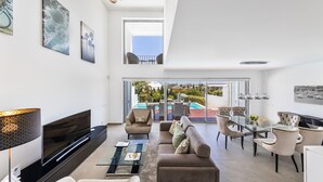 A modern living room with a flat-screen TV, comfortable seating, a glass coffee table, and a dining area with a glass top table and chairs.