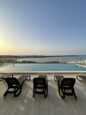 A rooftop pool area with three lounge chairs facing a view of the sea and distant cityscape. - Hotel VIU57 (Mellieha)