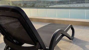 Een stoel op een betegeld terras met uitzicht op een wateroppervlak met boten en verre gebouwen.