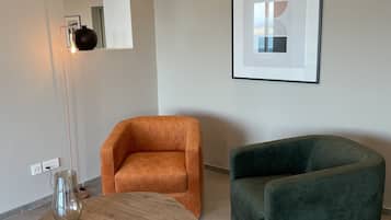 Una sala de estar moderna con una mesa redonda de madera, dos sillones, una lámpara de pie y una obra de arte abstracta enmarcada en la pared.
