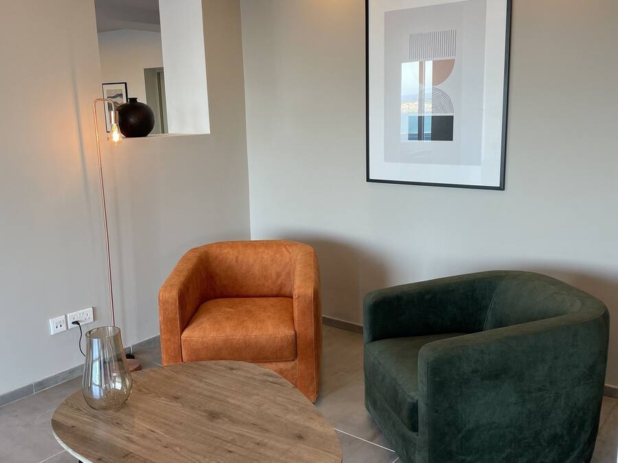 Una sala de estar moderna con una mesa redonda de madera, dos sillones, una lámpara de pie y una obra de arte abstracta enmarcada en la pared.
