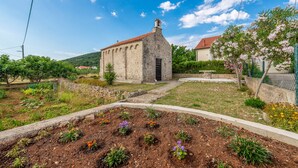 A stone building with a red-tiled roof, surrounded by a garden with various plants and flowers. - Little House by the Sea, Beachfront, Parking, WiFi (Preko)
