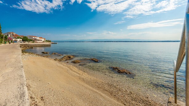 A coastal beach with clear water, a sandy shore, and a row of buildings in the background. - Little House by the Sea, Beachfront, Parking, WiFi (Preko)
