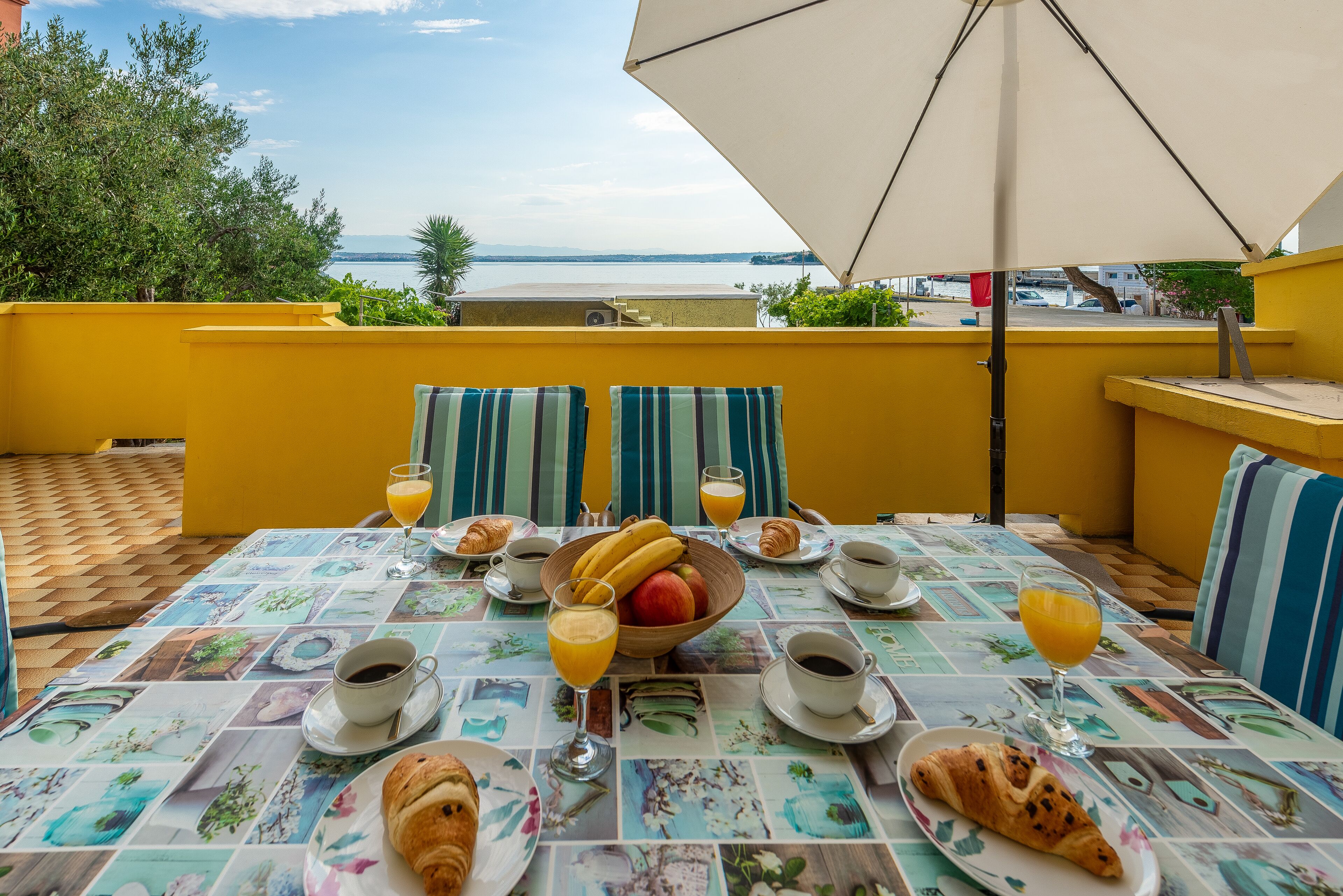 A breakfast table with a view of the sea, yellow walls, and striped cushions.